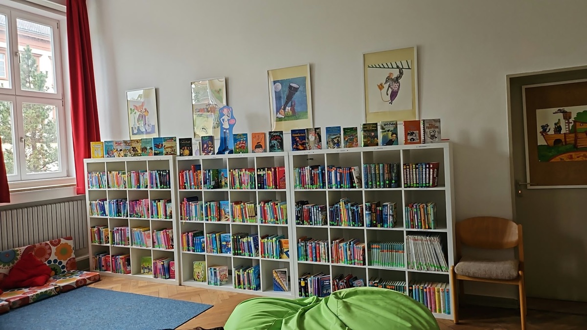 Der Leseraum der Schülerbücherei mit weißen Regalen voller Bücher, Bildern an der Wand und einem grünen Sitzsack